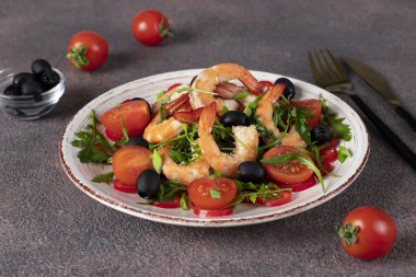 Karidesli salata, roka, vişneli domates ve kahverengi arka planda zeytinyağlı siyah zeytin.