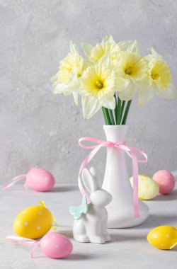 Vazoda nergisler, paskalya tavşanı ve açık gri arka planda renkli yumurtalarla dolu bir hayat. Kutlama kartı
