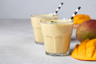 Açık gri arkaplanlı ve fotokopi alanı olan iki bardakta Mango Lassi. Taze Hint Lassi 'si yoğurttan, sudan, baharatlardan, mangodan ve buzdan yapılır.