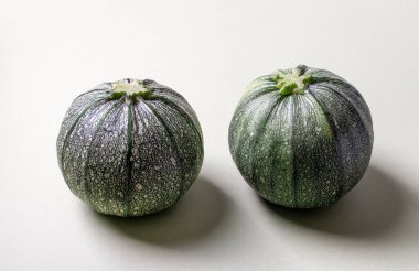 Açık arkaplanda gölgesi olan iki yuvarlak yeşil kabak. Yakın çekim.