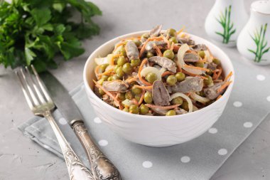 Tavuk kalpli salata, konserve bezelye, soğan ve havuç açık gri arka planda beyaz bir kasede.