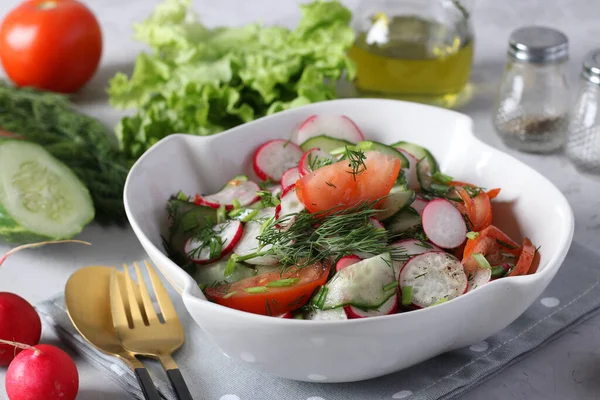 Салат з огірками, помідорами та редькою, одягнений в оливкову олію в миску з білим салатом на сірому фоні — стокове фото