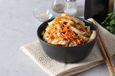 Kalamar, havuç ve salatalıklı salata, açık gri arka planda susam tohumları serpiştirilmiş.