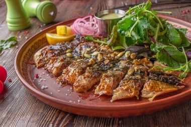 Ahşap masada soslu, soğanlı, limonlu ve yeşil salatalı ızgara uskumru.