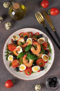 Karidesli salata, bıldırcın yumurtası, roka, vişneli domates ve kahverengi zemin üzerinde siyah zeytin.