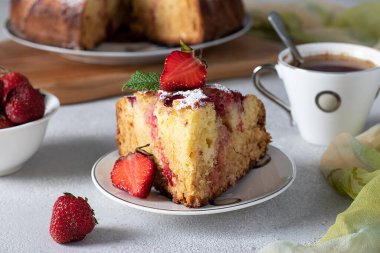 Bir dilim kesilmiş çilekli turta ve bir fincan kahve. Gri masada, yakın plan.