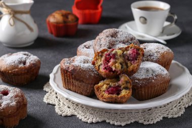 Muffins with cherries sprinkled with powdered sugar on a white plate on dark gray background