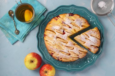 Ev yapımı elmalı turta, üzerine pudra şekeri serpiştirilmiş, açık mavi arka planda, üst manzara.