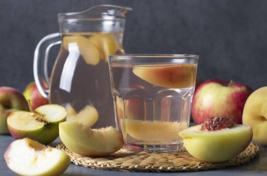 Bardaktaki şeftali ve elmalar ve koyu gri arka planda sürahi.