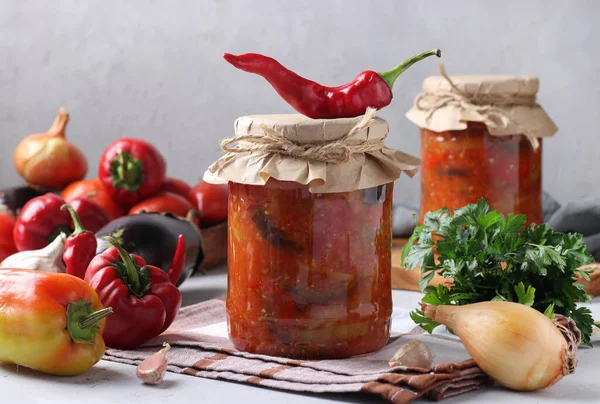 Ensalada de verduras con berenjena, zanahoria, pimientos, cebolla y tomates en frascos de vidrio sobre mesa gris — Foto de Stock