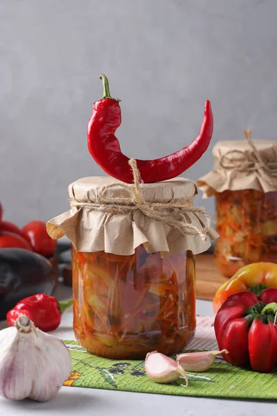 Salade de légumes avec aubergines, carottes, poivrons, ail et tomates dans des pots en verre sur fond gris — Photo