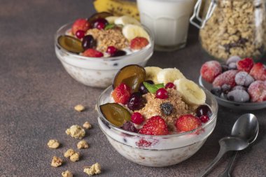 Doğal yoğurtlu gevrek müsli, donmuş böğürtlen, meyve ve fındıklar kahverengi arka planda iki cam kasede, sağlıklı kahvaltı.