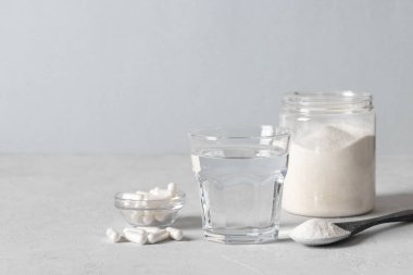 Kolajen tozu kaşıkta, kolajen kapsülleri, bir bardak su ve açık mavi arka planda bir kavanoz toz. Sağlıklı ve yaşlanmayı önleyici kavram