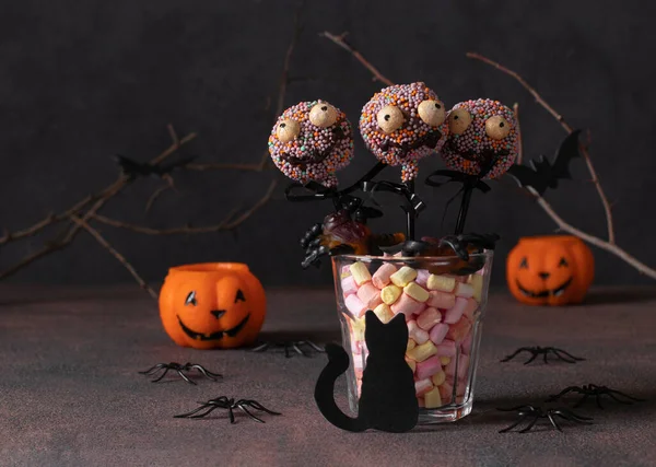 Homemade Halloween cake pops monsters with dark chocolate on brown background. Sweets for kids on Halloween party