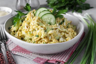 Tavuklu salata, Çin lahanası, salatalık, haşlanmış yumurta ve peynir açık gri arka planda, yakın planda.