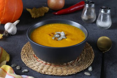 Koyu gri arka planda kabak tohumlu kalın balkabağı kremalı çorba.