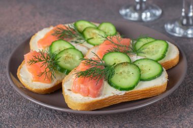 Kahverengi zemin üzerinde tuzlanmış somon, salatalık ve dereotlu sandviçler. Atıştırmalık şenlik, yakın çekim.