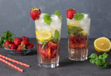 Nane aromalı soğuk, parlak çilekli mojito kokteyli, limon dilimleri ve koyu gri arka planda buz küpleri.