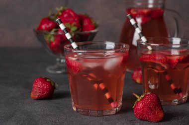 İki bardakta soğuk çilek kompostosu, pipet ve kahverengi arka planda sürahi.