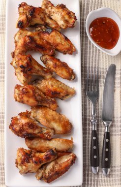 Beyaz tabakta ızgara tavuk kanadı, domates sosu ve çatal bıçak takımı.