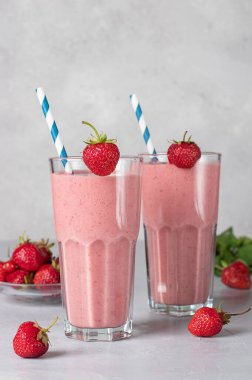 İki bardakta çilekli ev yapımı milkshake ve arka planda pipet içmek.