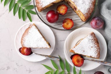 Ev yapımı erikli turta üzerine pudra şekeri serpiştirilmiş. Açık arkaplandaki tabaklarda kesilmiş parçalar. Üst görünüm