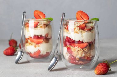 Bisküvi, mascarpone peyniri ve bademle birlikte bardakta çilekli tatlı. Açık gri arka planda çocuk partisi için lezzetli bir tatlı.