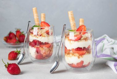 Bisküvi, mascarpone peyniri, badem ve kurabiye tüpleriyle katmanlı çilekli tatlı. Çocuklar için lezzetli tatlı Açık gri arka planda parti