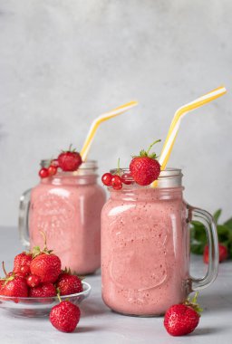 Çilekli ev yapımı smoothie ve uzun gözlüklü kırmızı frenk üzümü açık gri arka planda pipet içme, dikey format