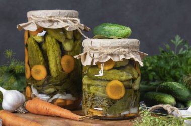 Ev yapımı salatalık turşusu, havuç, sarımsak, defne yaprağı ve koyu gri arka planda iki kavanozda dereotu.
