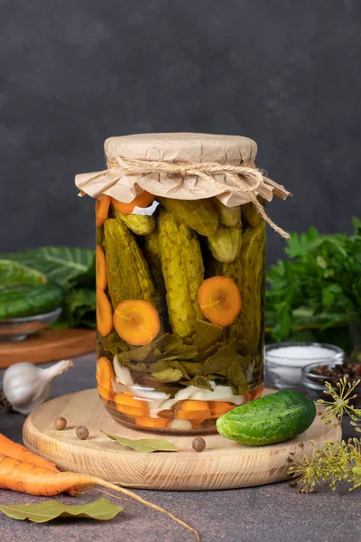 Homemade pickled cucumbers with carrots, garlic, bay leaves and dill in glass jar on gray background, Vertical format