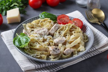 Tagliatelle pasta with chicken and cheese, served with cherry tomatoes and basil on dark gray background