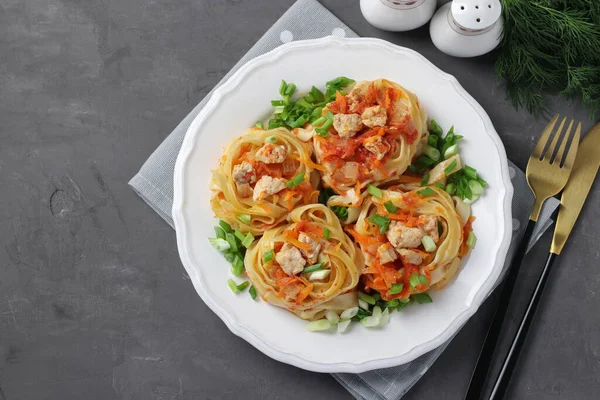 Tagliatelle pasta with turkey, vegetables and tomato sauce on a white plate on dark gray background, Top view