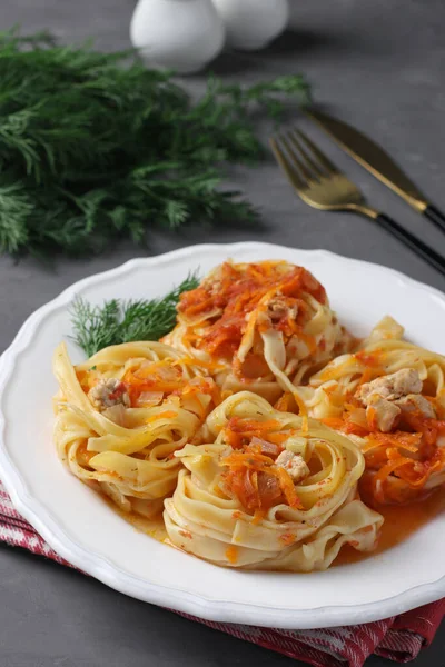 Tagliatelle pasta with turkey, vegetables and tomato sauce on a white plate on gray background