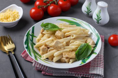 Penne pasta with chicken fillet and cheese in plate, served with cherry tomatoes on dark gray background