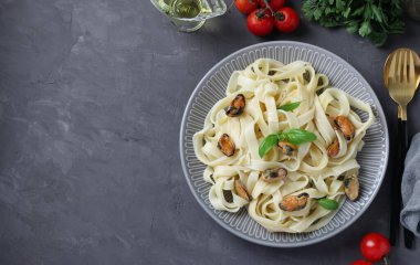 Tagliatelle pasta with mussels and basil on plate on dark gray background. Copy space