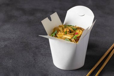 Noodles with seafood and vegetables in takeaway box on dark gray table