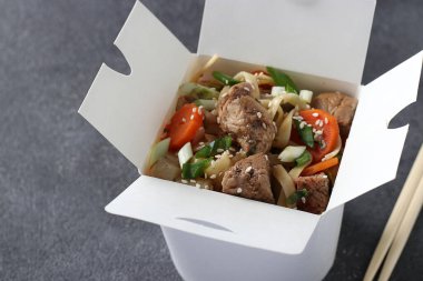 Noodles with pork and vegetables in take-out box on gray table, Close-up
