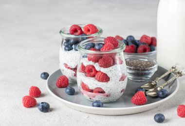 Chia pudding with blueberry and raspberry in two glass jars on light gray background. Healthy food