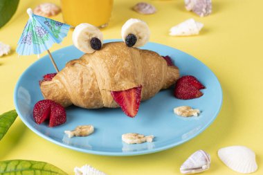 Fun food for kids - crab shaped croissant with strawberry and banana on blue plate on yellow background