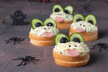 Cucumber, sausage, black olives, egg and melted cheese sandwiches in the shape of frogs - creative idea for Halloween appetizer