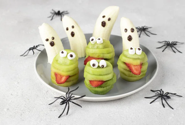 Spooky banana ghosts monsters and green kiwi monsters for Halloween party on gray background. Minimal Halloween Fruit Serving Idea