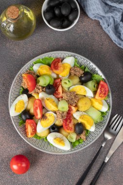 French salad Nicoise with tuna, boiled potatoes, egg, black olives, cucumbers, tomatoes and lettuce, Top view on brown background