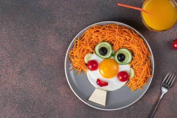 Fun Food for kids - smiling face boy made from fried eggs, carrot, cucumbers and cherry tomatoes on gray plate. Creative healthy breakfast for children