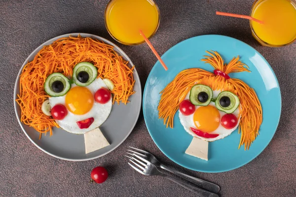 Fun Food for kids - smiling faces boy and girl made from fried eggs, carrot, cucumbers, crerry tomato, black olives on plates. Creative healthy breakfast for children