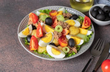 Fransız salatası Nicoise, ton balığı, haşlanmış patates, yumurta, siyah zeytin, salatalık, domates ve marul kahverengi arka planda, yüksek açı.