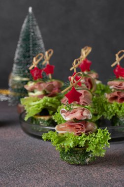 Prosciutto, salatalık, salatalık, marul yaprağı ve kahverengi arka planda dolmalık biber yıldızlarından şekilli Noel ağaçları.