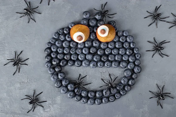 Monster of blueberries, plums and marshmallows for Halloween party on gray background, flat lay