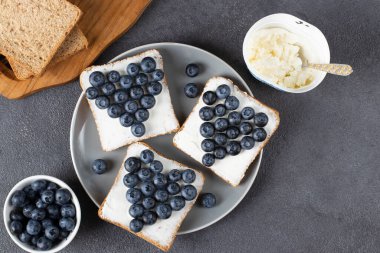 Kalp şeklinde krem peynir ve çavdar ekmekli yaban mersinli sandviç. Gri tabakta tost, üst manzara.