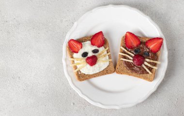 Çilekli, muzlu, krem peynirli ve çikolatalı çocuklar için gri arka planda beyaz tabakta iki tatlı tost.